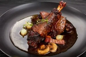 close-up of a portion of Coq Au Vin - tasty chicken braised with wine, herbs, mushrooms and vegetables served on black plate, authentic french recipe
