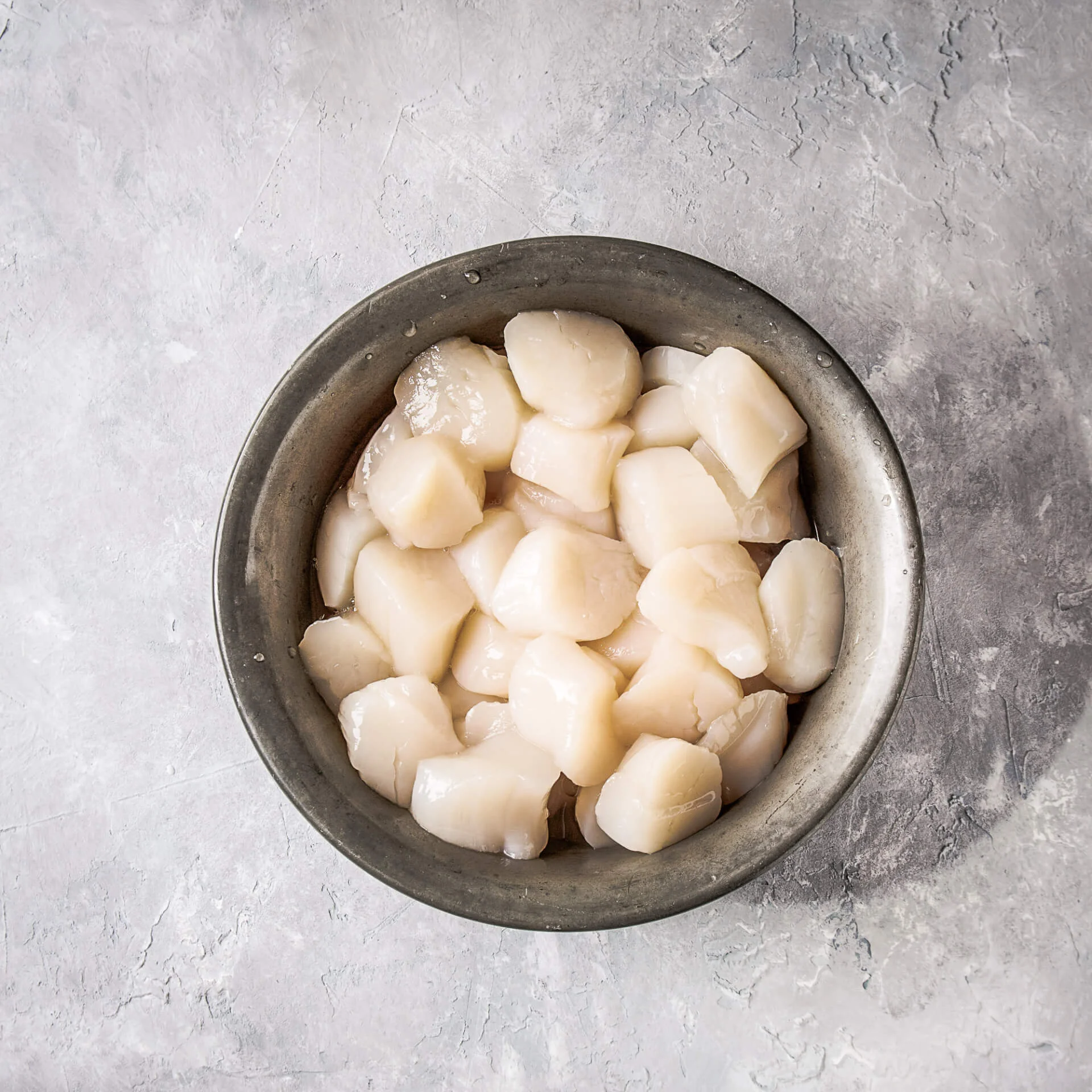 Raw uncooked scallops for coquilles saint jacques, shown in vintage metal bowl over gray texture background. Top view.