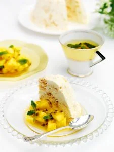 White plate and spoon topped with iced ginger meringue and diced tropical fruit. Cup of tea in yellow cup.