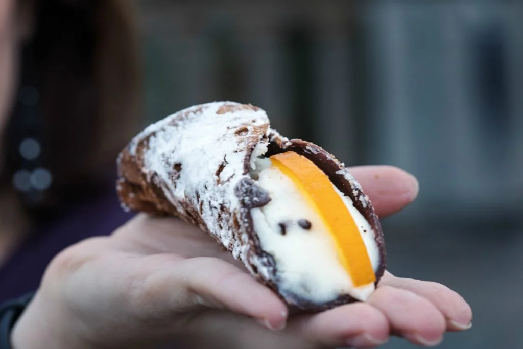 Cannoli on a hand with blurry background. Italian pastries of the Sicily region. Sicilian or Italian cuisine.
