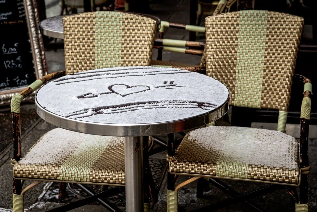 Table of Parisian street cafe covered with snow and heart shaped drawing