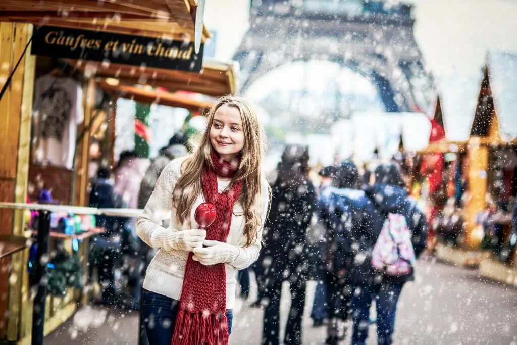 Happy young girl with caramel apple on a Parisian Christmas market with the Eiffel tower in the background during snowfall