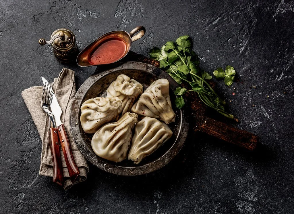 Georgian dumplings Khinkali with meat and tomato spicy sauce satsebeli on dark stone background